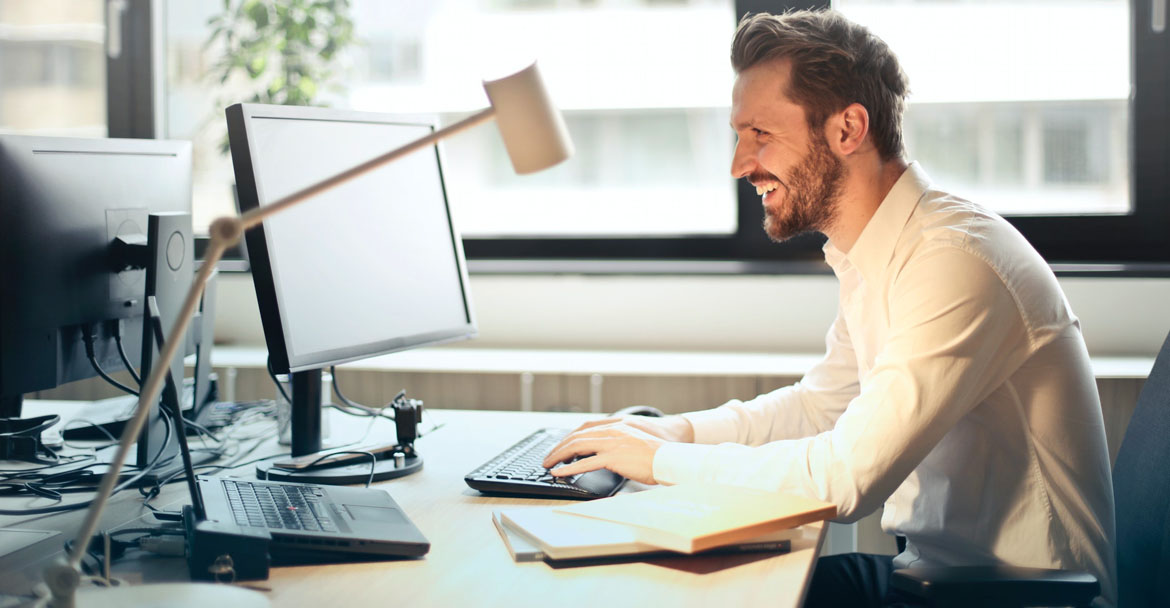 hombre de negocios sonriendo junto con su ordenador portatil en su oficina mientras trabaja