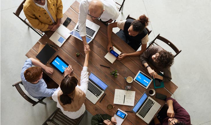 imagen de un plano cenital que muestra como trabajan en una mesa central 8 personas de una misma empresa, todos juntos.
